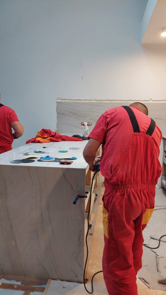 Dwóch fachowców poleruje kamienny blat w trakcie montażu — widoczny etap precyzyjnej obróbki.