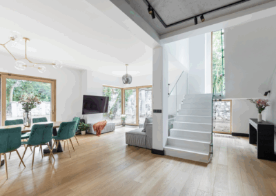 Klatka schodowa z białymi schodami z konglomeratu i szklaną balustradą, otwarta na światło i ogród.