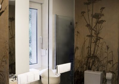 Łazienka w domu letniskowym z dużym lustrem, tapetą roślinną i drewnianym blatem — wnętrze w duchu zero waste.