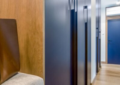 Przedpokój w apartamencie na Ursynowie — granatowa zabudowa, siedzisko i drewniana podłoga w nowoczesnym wnętrzu.