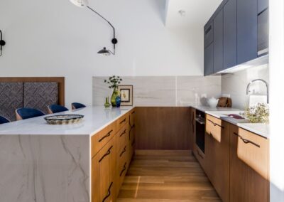 Aneks kuchenny w apartamencie na Ursynowie — marmurowy blat, drewniana zabudowa i ergonomiczny układ w nowoczesnym wnętrzu.