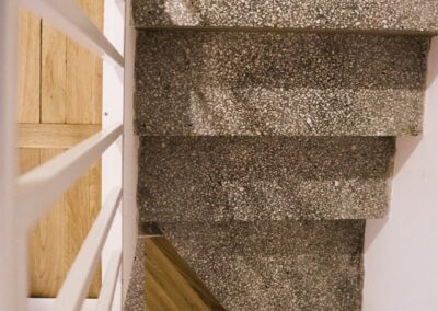 Widok z góry na schody z kamienia i drewna w domu letniskowym z lat 80., z białą balustradą i minimalistycznym detalem.