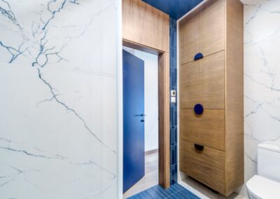 Łazienka na parterze apartamentu na Ursynowie — drewniana zabudowa, niebieskie akcenty i marmurowe płytki w nowoczesnym wnętrzu.