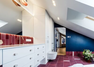 Łazienka rodziców na antresoli — biała zabudowa, czerwone płytki i naturalne światło w apartamencie na Ursynowie.