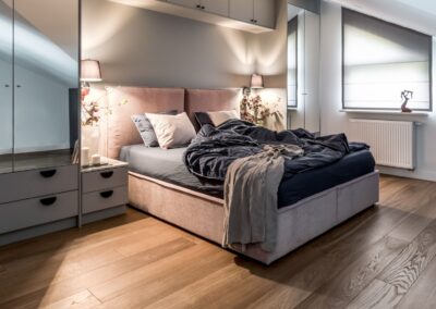 Sypialnia w apartamencie na Ursynowie — zabudowa nad łóżkiem, lustrzana szafa i stonowana kolorystyka.