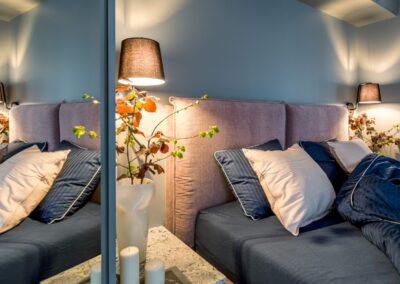 Detal sypialni w apartamencie na Ursynowie — tapicerowany zagłówek, granatowa pościel i oświetlenie punktowe.
