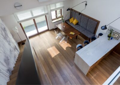 Widok z antresoli na salon z aneksem — wyspa kuchenna, ławka jadalniana i mural w apartamencie na Ursynowie.